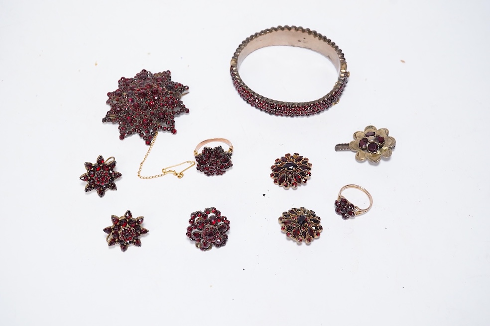 A suite of garnet and paste jewellery, comprising: a brooch, 5cm diameter; a bangle, inner circumference 16cm; two rings, sizes I and M; a pair of earrings, and a single earring, each set with rose-cut garnets; and a pai